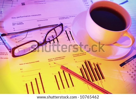 Late night checking financial performance.  Coffee for a caffeine boost, glasses and pencil on financial papers.  Warm tones.