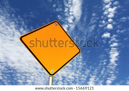 Blank yellow road sign, against brilliant blue sky with scattered clouds.