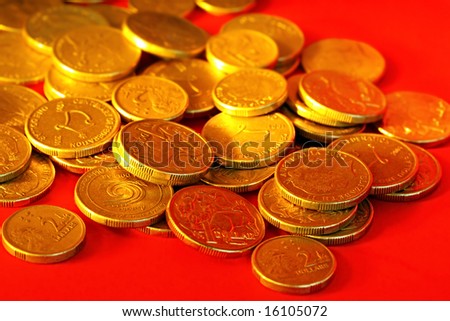 Golden Australian one and two dollar coins, scattered on red background.
