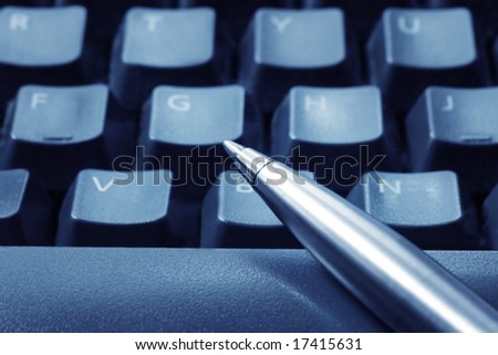 Ballpoint pen resting on computer keyboard.  Blue tone, focus on pen tip.