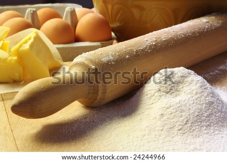 Baking in early morning light.  Old rolling pin and sifted flour on a board, with butter, eggs and vintage bowl.