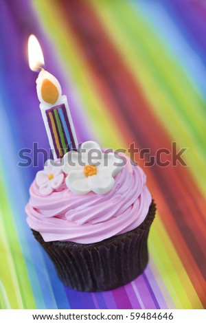 Cupcake with fancy candle, over vibrant striped background.  Chocolate cupcake with pink frosting and flowers.