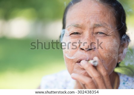 MANDALAY, MYANMAR - JULY 30, 2014 old wrinkled Asian woman smoking traditional tobacco. Bagan, Myanmar.