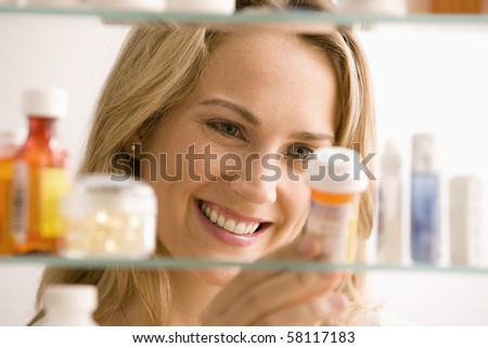 A young woman is looking through her medicine cabinet and smiling.  Horizontal shot.