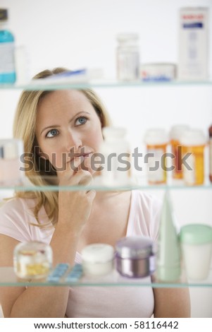 A young woman is looking through her medicine cabinet.  Vertical shot.