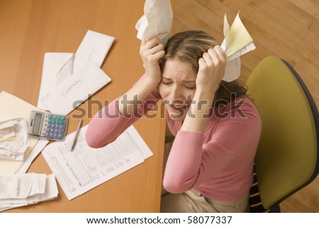 A young woman is paying bills at her desk and has her eyes closed from stress.  Horizontal shot.
