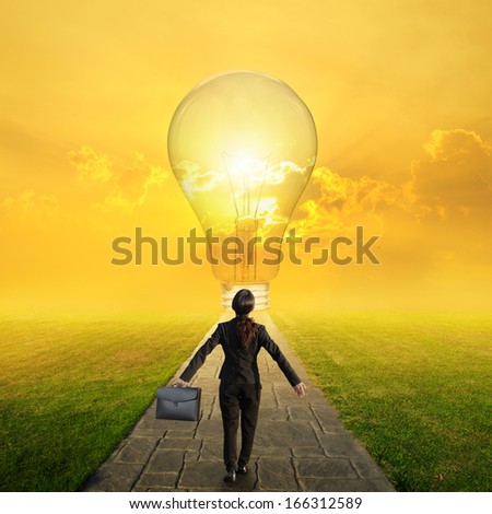 Relax business woman holding bag on Concrete road to Big idea bulb in Grass fields and sunset