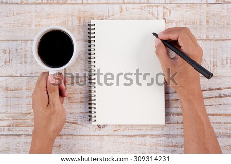 Cup of hot coffee and man hand writing notebook  on white wood table background.copy space