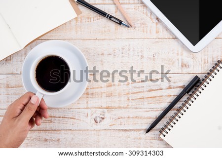 Tablet phone notebooks pen and Man hand holding  Cup of hot coffee  on wood table background.copy space.