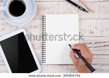 Cup of hot coffee and man hand writing notebook on wood table background.copy space