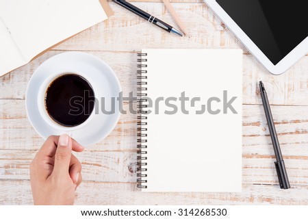Man hand holing Cup of hot coffee and  notebook on wood table background.copy space