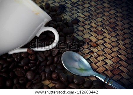 white cup of hot coffee and tea spoon with fresh coffee bean display on wood desk studio pack shot low key light