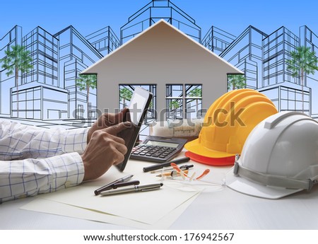 hand of architect working on computer tablet  with construction industry and engineer working tool on top of table against home out line and sketching of modern building perspective