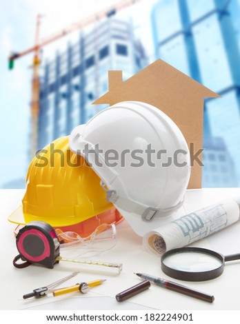 safety helmet blue print plan and construction equipment on architect ,engineer working table with building construction crane background use for construction industry business and civil engineering