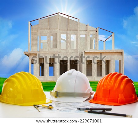 hard hat of engineering on working table with plan and writing tool against house structure in construction