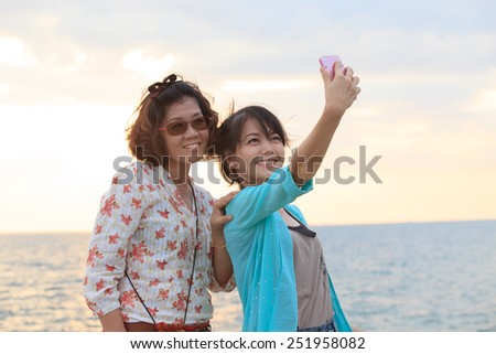 two sister take a photo,selfie by smart phone beside sea beach with happy emotion