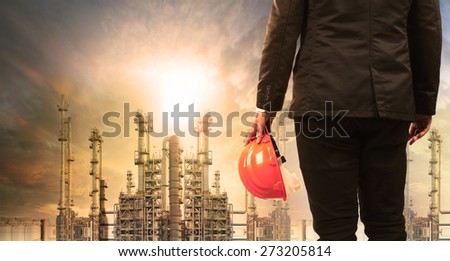 engineering man with safety helmet standing in industry estate against sun rising above oil refinery plant