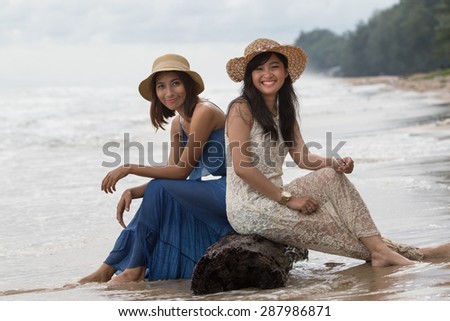 portrait of young beautiful asian tan skin  woman wearing fashion straw hat sitting on wood lock at sea beach with relaxing emotion