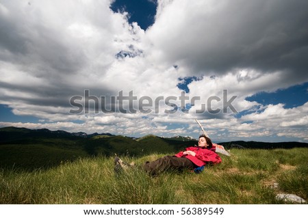 Women is laying down on the grass on top of mountain peek, relaxing from everyday's troubles with dramatic clouds over her head