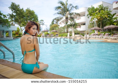 Sexy asian girl in blue bikini sitting near swimming pool