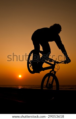 young man performing bike tricks at sunset
