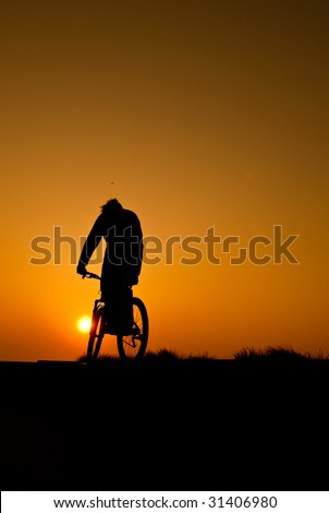 silhouette of a young adult riding a bike at sunset