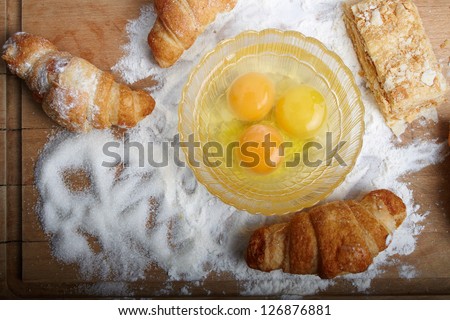The broken eggs and baking on the wooden board poured by a flour and sugar.