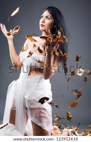 Beautiful young brunette woman spreading hands to falling leaves
