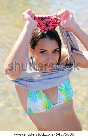 Young woman taking off swim suit cover with bikini underneath