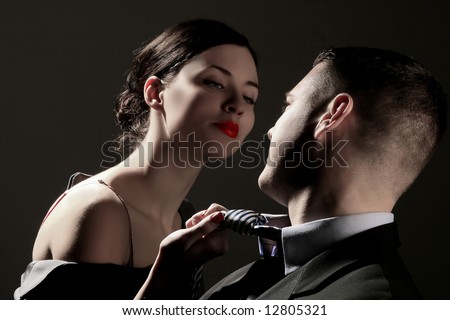 a business lady is pulling man\'s tie on the black