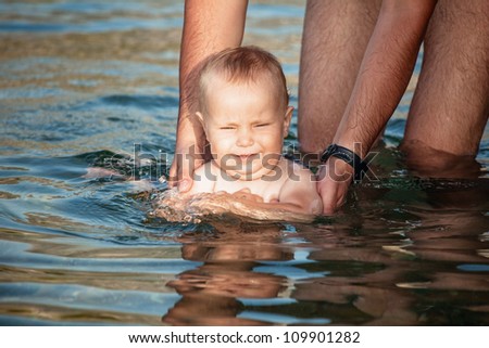 Father teaches baby son to swim in the sea