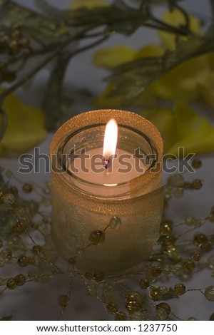 Small lit candle in a votive cylinder surrounded by beads and branches