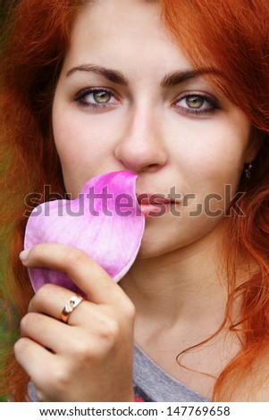 Beautiful young ginger haired girl smelling a pink magnolia petal