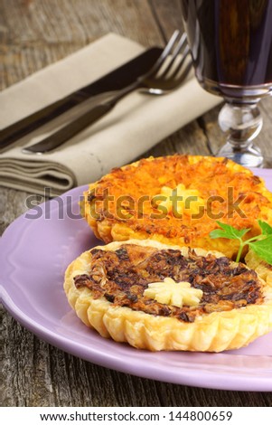 Two mini vegetarian quiches one with trevisano chicory and one with carrots on a pink plate and a glass of red wine over a wooden background