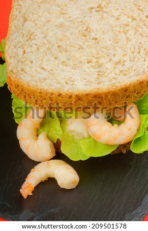 Shrimps sandwich with lettuce on a slate tray over a red background