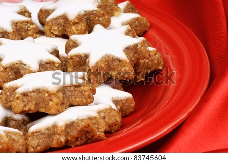 Close-up of some cinnamon star cookies (in german Zimtsterne), typical german and swiss Christmas cookies on a red plate over a red background.