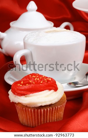 Valentine\'s day romantic breakfast composed of cupcake, with a red buttercream heart, and cappuccino. In the background a sugar bowl. Selective focus.