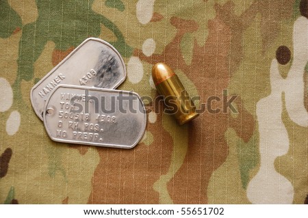 US dog tags and .45 caliber cartridge on multicam background