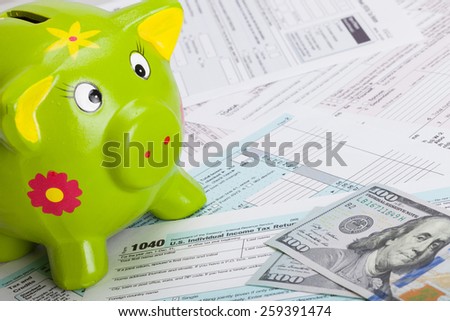 Hundred USA dollars banknote and piggy bank over US tax form