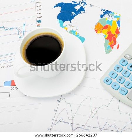Coffee cup and calculator over world map and stock charts - close up shot