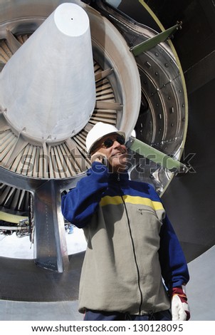 airplane mechanic talking in phone with jumbo jet-engine in background