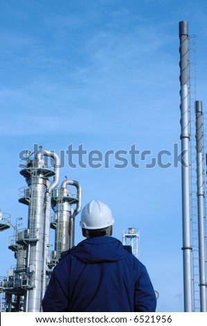 engineer in hard-hat overlooking refinery, pipelines and pipes