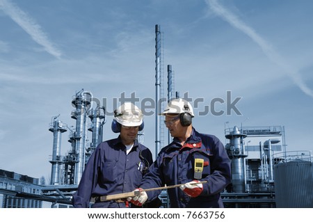 engineers wearing hard-hats in front of oil and gas refinery, background in blue toning