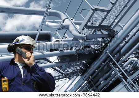 engineer in hard-hat with large refinery pipelines in background, blue toning background
