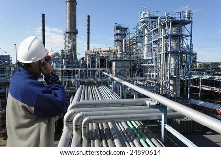 oil-worker in foreground pointing at oil and gas refinery in background
