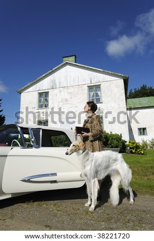 lady in fur-coat and dog going towards a vintage car