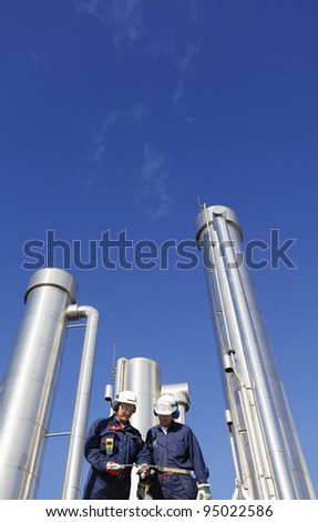 hardhat workers inside refinery, oil and gas pipes in background