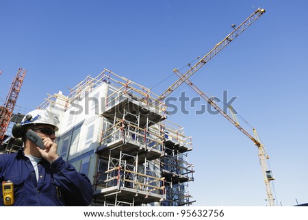 construction worker talking in phone, large site in background, cranes, scaffolding and machinery