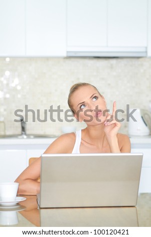 Thinking woman sitting at her laptop computer in her kitchen enjoying something she has just read over the internet