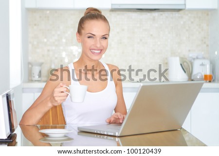 Laughing woman sitting at her laptop computer in her kitchen enjoying something she has just read over the internet